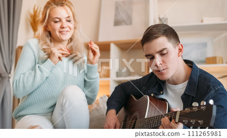 Music leisure. Couple chill. Good time together. Cheerful romantic man playing guitar for singing joyful woman on couch at home in living room. 111265981