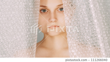 Plastic contamination. Polyethylene waste. Garbage recycling. Serious upset woman face portrait behind bubble wrap dangerous material packaging. 111266040