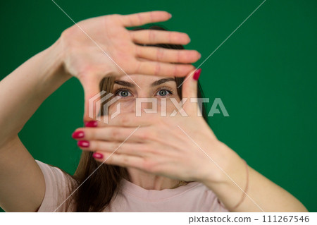 beautiful girl framing her face with her hands different emotions of a young girl on a green background chromakey beautiful facial features real people pink T-shirt white skinned. European beautiful girl framing her face with her hands different emotions of a young girl on a green background chromakey beautiful facial features real people pink T-shirt white skinned. European 111267546