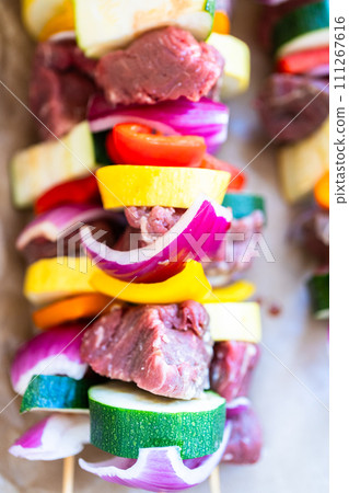 Raw skewers with beef and fresh veggies, wrapped in butcher brown paper, await grilling. 111267616