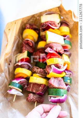 Raw skewers with beef and fresh veggies, wrapped in butcher brown paper, await grilling. 111267778
