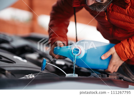 Pouring winter washer fluid into car reservoir during winter, protecting it from freezing. 111267795