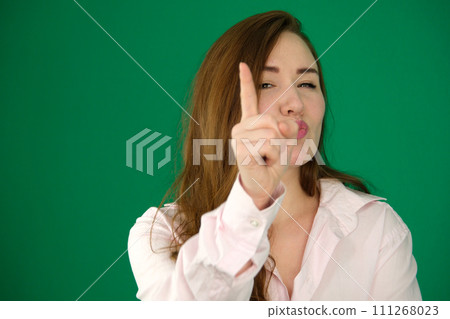 Portrait of a composed young Asian woman wrapped in a white towel against a soft green background, saying no by wagging her finger. Portrait of a composed young Asian woman wrapped in a white towel against a soft green background, saying no by wagging her finger. 111268023