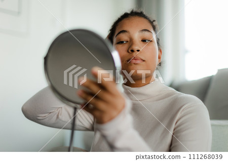 Portrait of beautiful curvy woman, looking at small round makeup mirror at home. Portrait of beautiful curvy woman, looking at small round makeup mirror at home. 111268039