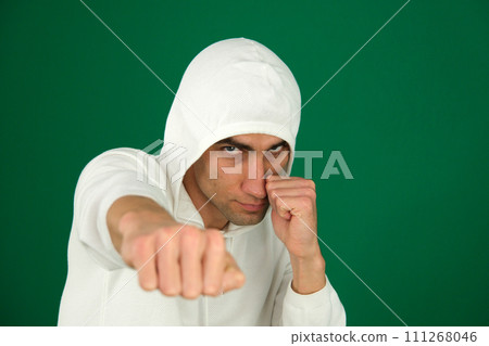 a guy in a white hoodie on a green chromakey background hits the camera with his fist a stern angry look defense attack a guy in a white hoodie on a green chromakey background hits the camera with his fist a stern angry look defense attack 111268046