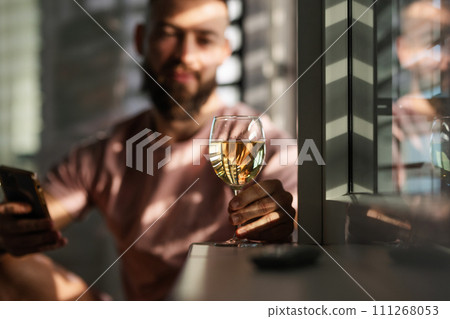 Young man looking at glass with white wine, New Year's resolutions, drink less alcohol healthy lifestyle without alcoholic drinks. 111268053