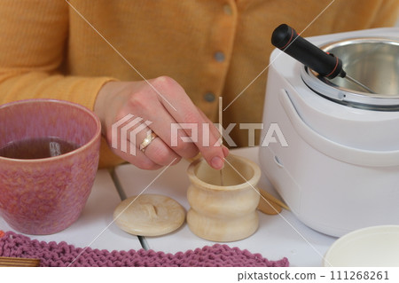 The process of making a massage candle using ingredients oils and wax measure weigh stir add close-up of women's hands. food thermometer measure wax temperature women's party women witches witchcraft 111268261