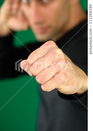 Portrait of bearded man standing with boxing fists and ready to attack or defence, looking with angry face, looking at camera with aggression. Indoor studio shot isolated on blue background. 111268394