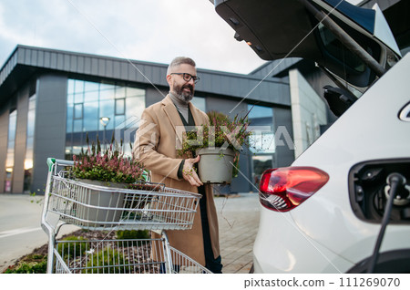 Man charging electric car before going to shopping. Public charging station in front of shop building, supermarket. Charging while shopping. Man charging electric car before going to shopping. Public charging station in front of shop building, supermarket. Charging while shopping. 111269070