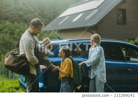 Family with electric car standing in front their house with solar panels on roof. Solar energy and sustainable lifestyle of young family. Concept of green energy and sustainable future for next 111269141