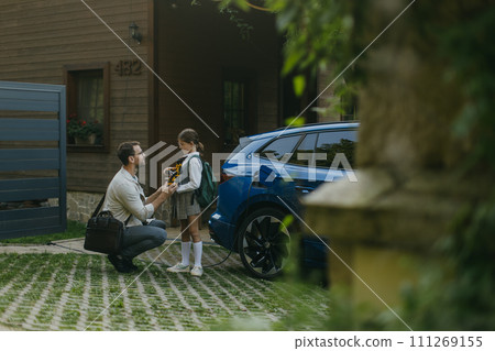 Father handing girl her science project for school science fair, robotic arm. Electric car is charging before going to school and work. Concept of young girls in science. Father handing girl her science project for school science fair, robotic arm. Electric car is charging before going to school and work. Concept of young girls in science. 111269155
