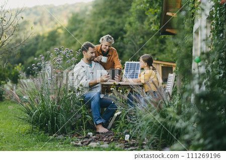 Parents with daughter sitting outdoors in garden, with model of solar panel, learning about solar energy. Solar energy and sustainable lifestyle of young family. 111269196