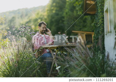 Man working in the garden on laptop, phone calling. Businessman working remotely from outdoor homeoffice, thinking about new business or creative idea. 111269201
