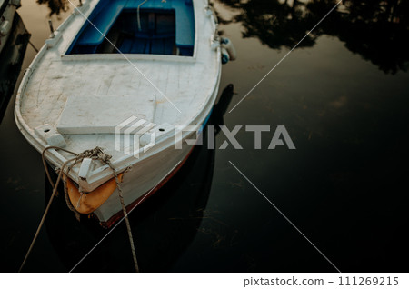 Small boat on calm water, moored in the harbor during sunset. 111269215
