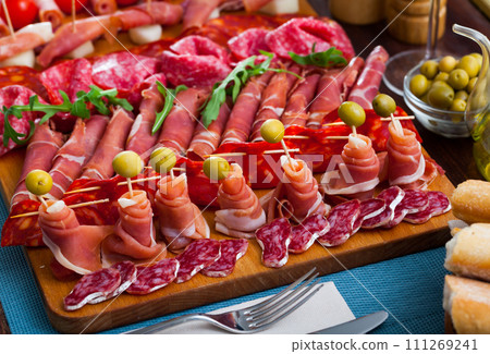 Slicing sausages and ham with cherry tomatoes and olives on board 111269241
