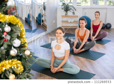Young women practicing yoga in gym decorated with Christmas tree Young women practicing yoga in gym decorated with Christmas tree 111269553