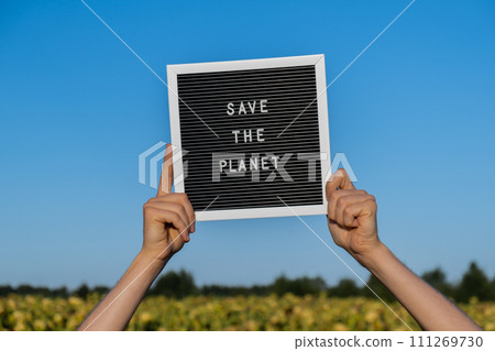 Hands of protester with text SAVE THE PLANET on black board on background of sunflower field. Reuse reduce recycle concept. Protesting for nature Climate strike volunteer protest against earth Hands of protester with text SAVE THE PLANET on black board on background of sunflower field. Reuse reduce recycle concept. Protesting for nature Climate strike volunteer protest against earth 111269730