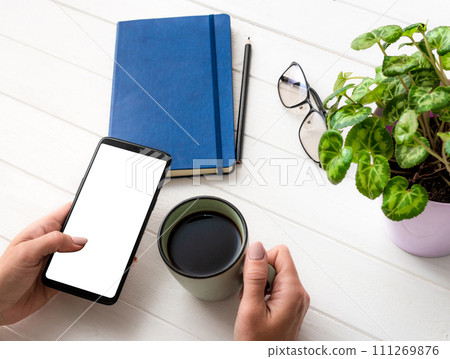 Top view of girl using smartphone and holding coffee mug at working place Top view of girl using smartphone and holding coffee mug at working place 111269876