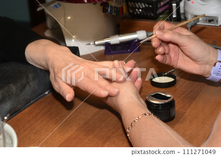 The manicurist applies colorless varnish with a thin brush. 111271049