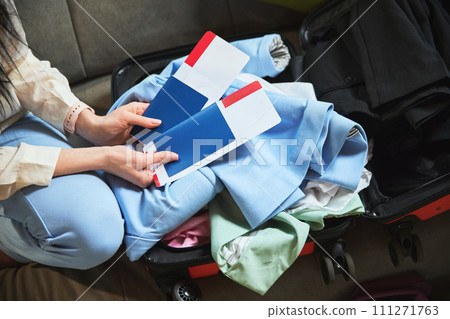 Focus on passport and ticking. Woman holding travel attributes above suitcase with clothes. Preparation for trip Focus on passport and ticking. Woman holding travel attributes above suitcase with clothes. Preparation for trip 111271763