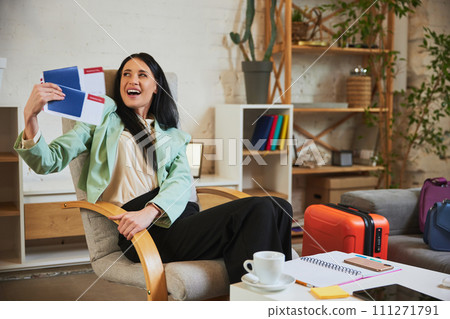 Happy smiling businesswoman sitting at home and showing passport with tickets, expressing excitement about upcoming vacation 111271791