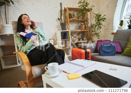Happy, joyful young woman, employee sitting in office, holding plane tickets, talking on phone and expressing excitement about upcoming trip Happy, joyful young woman, employee sitting in office, holding plane tickets, talking on phone and expressing excitement about upcoming trip 111271796