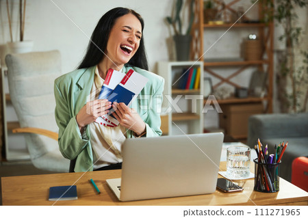 Happy smiling businesswoman sitting in modern office, planning vacation, showing plane tickets. Online purchase and booking Happy smiling businesswoman sitting in modern office, planning vacation, showing plane tickets. Online purchase and booking 111271965