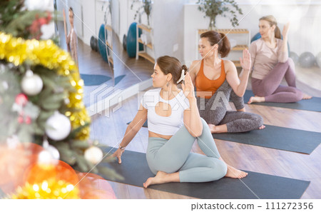 Girl teacher conduct yoga lesson for girls and doing Lord of fishes pose in New Year atmosphere. Girl teacher conduct yoga lesson for girls and doing Lord of fishes pose in New Year atmosphere. 111272356