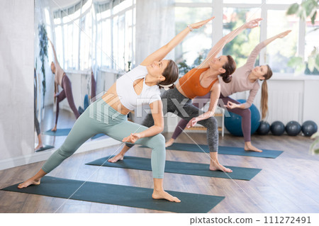 Women practicing warrior pose of yoga on mat in fitness room 111272491