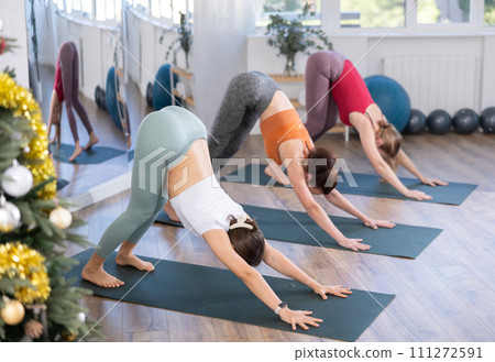 Girl teacher lead yoga lesson for girls and doing dog face down pose in New Year atmosphere. 111272591