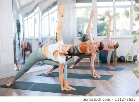 Young woman performing Utthita Parsvakonasana during group yoga workout 111272622