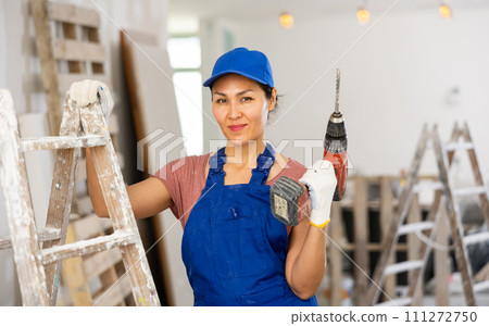 Smiling woman builder holding drill, repair works in apartment Smiling woman builder holding drill, repair works in apartment 111272750