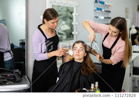 Professional female stylists making hairstyle and makeup to young woman 111272828