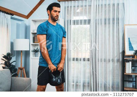 Athletic body and active sporty man lifting kettlebell at gaiety home exercise. 111273707