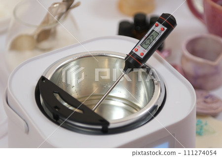 The process of making a massage candle using ingredients oils and wax measure weigh stir add close-up of women's hands. food thermometer measure wax temperature women's party women witches witchcraft 111274054