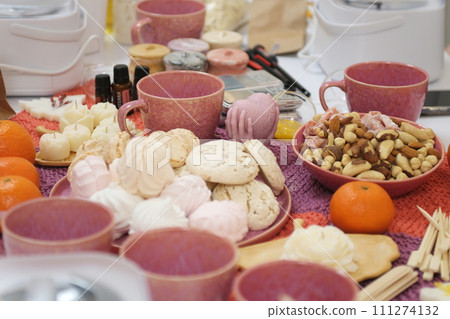 marshmallow tea cups delicious snack nuts dried fruits and tangerines on the table sweets good presentation healthy self-care treats for guests on a wicker woolen tablecloth napkin 111274132