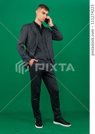 emotions of a handsome man guy on a green background chromakey close-up dark hair young man. phone in hand talk dial SMS online call gadget boss work advertising 111274223