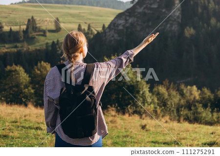 Woman hiker with backpack open arm at mountain peak. Travel and active lifestyle concept. 30s girl enjoying valley view from top of a mountain, outdoor activities, back view. Morning time 111275291