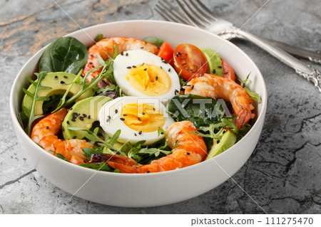Homemade salad for weight loss with shrimp, avocado, arugula, spinach, tomatoes and boiled eggs close-up in a bowl. Horizontal 111275470