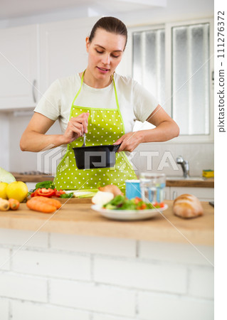 Woman in apron cooking delicious soup in pot in kitchen 111276372