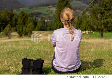Back view of Woman in active trekking clothes having a halt after hiking. Travel and active lifestyle concept. 30s girl enjoying valley view from top of a mountain, outdoor activities 111276528