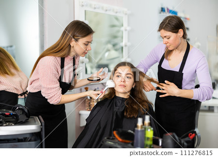 Make-up artist and a hairdresser serve a young female client 111276815