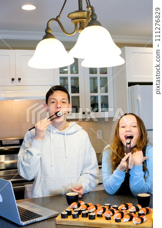 guy and girl in kitchen eating sushi, watching a movie, talking, friends, communicating, having fun. people, leisure, eating, couple with smartphones taking picture of sushi at restaurant 111276829