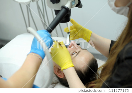 dentist doctor and nurse treat teeth to a patient using a microscope Female patient opening her mouth under the dental microscope and a professional dentist holding tools 111277175