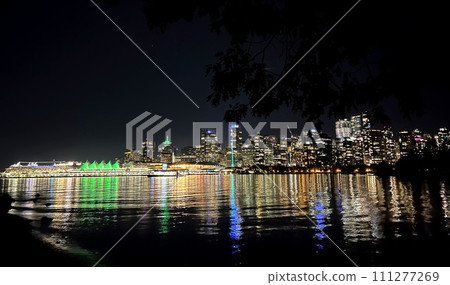 Mirror reflection of the whole city in the ocean Dark night in Canada Vancouver view from ocean luminous building Canada Place sails in green Skyscrapers glow with many lights reflected in the water 111277269