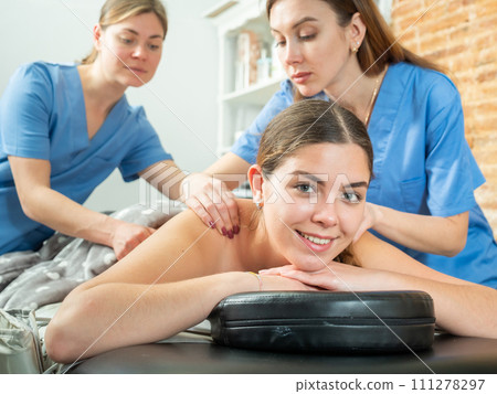 Young woman enjoying relaxing massage from two masseurs 111278297