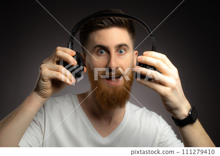 Young bearded man listening to music with headphones on black background 111279410