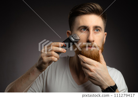 Handsome bearded man cutting his own hair with a clipper Handsome bearded man cutting his own hair with a clipper 111279417