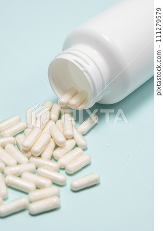 White medicine capsules spilled out of a jar on light blue background close-up. White medicine capsules spilled out of a jar on light blue background close-up. 111279579