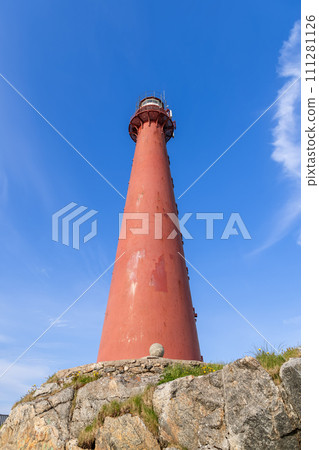 Lofoten's Andenes Lighthouse atop rugged rocks against summer blue sky, Norway's natural beauty 111281126